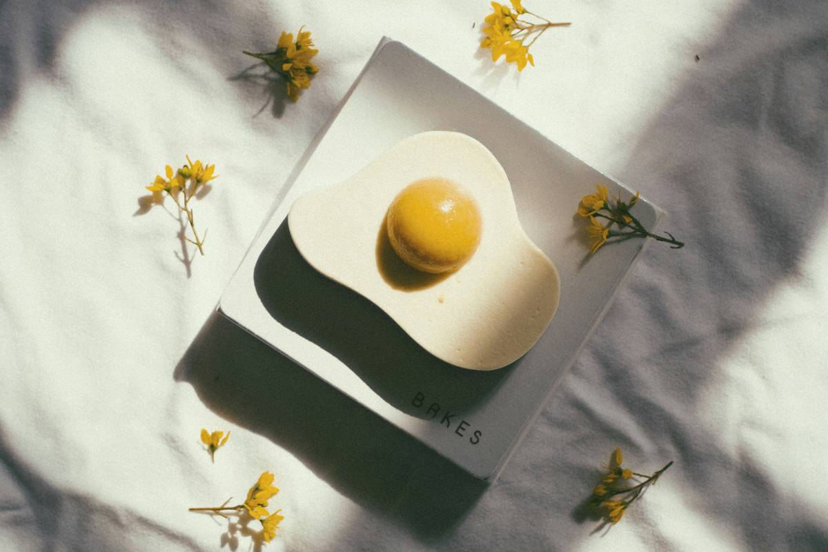 microwave egg poacher tool equipment in white ceramic cup with silicone lid, resting on a marble countertop beside a fork and fresh herbs